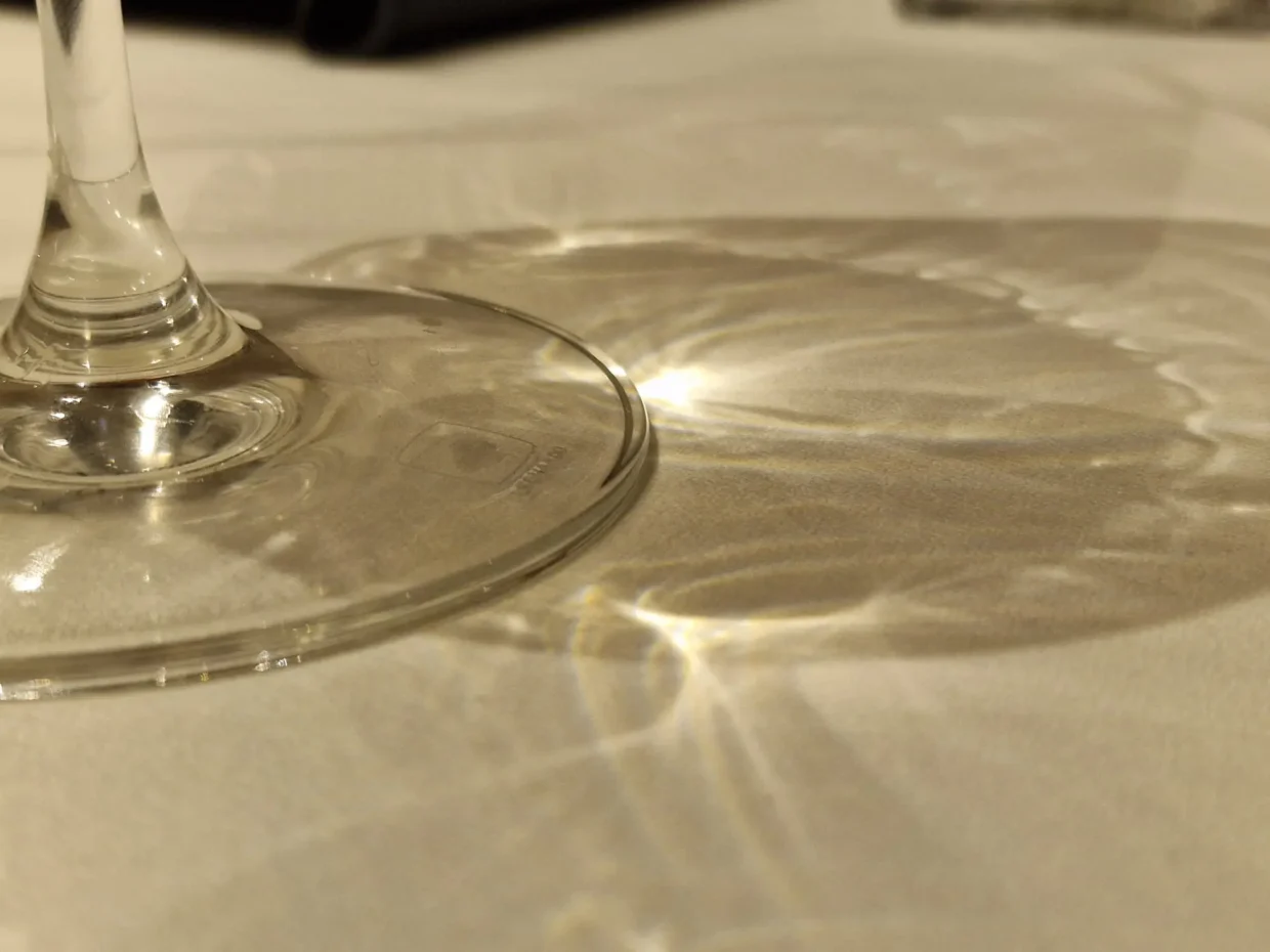 Fuß Eines Weinglases Auf Einer Weißen Tischdecke Mit Warmen Lichtreflexionen